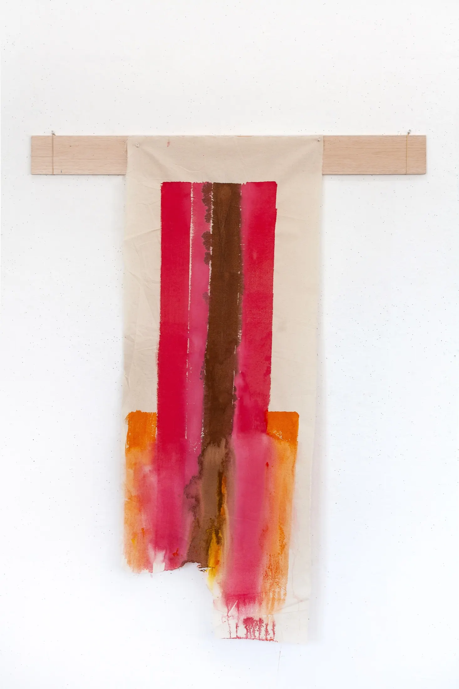 Long cream fabric draped over a horizontal wooden slat on a white wall, painted with vertical red, pink, brown, and orange bands.